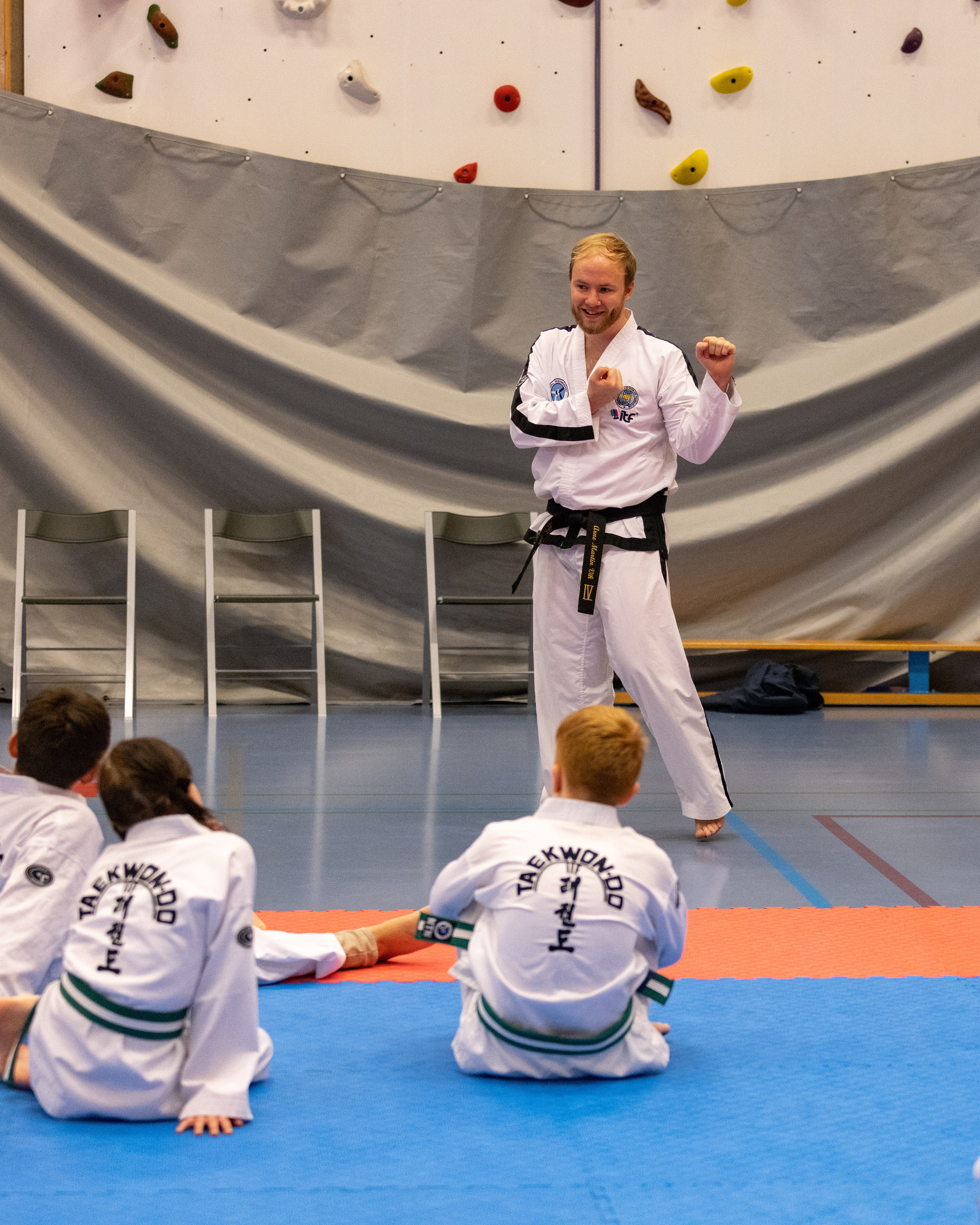 Mann i Taekwon-Do drakt står foran barn som sitter og ser på.